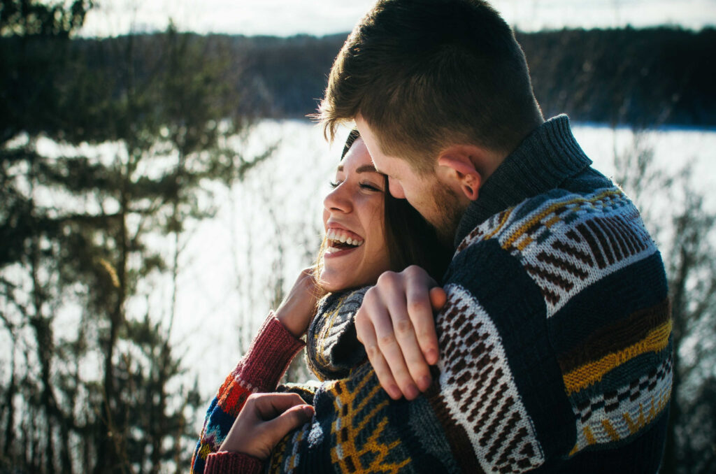 Young man in a sweater hugs a girl from behind